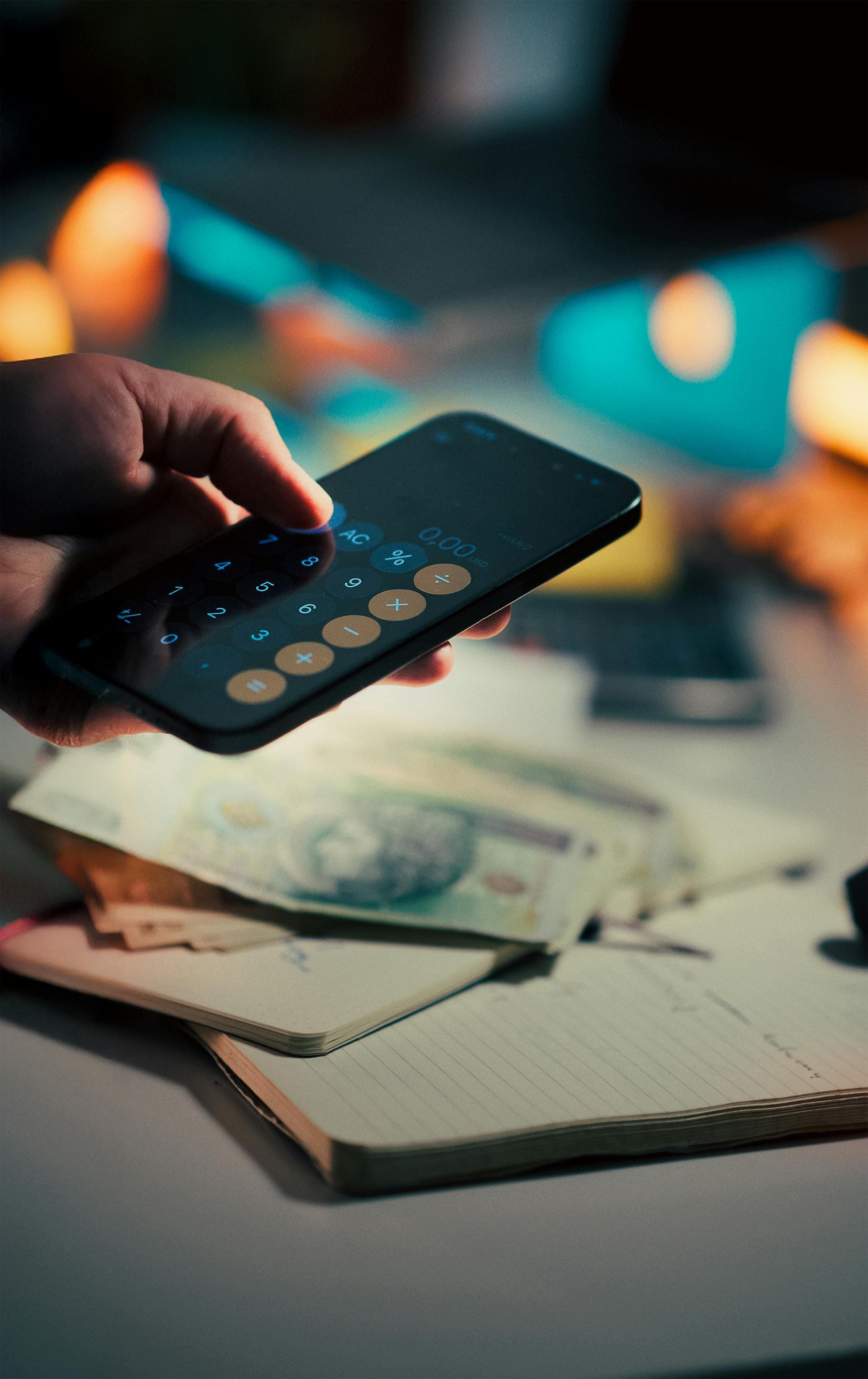 Phone calculator over cash and a notebook on a desk.