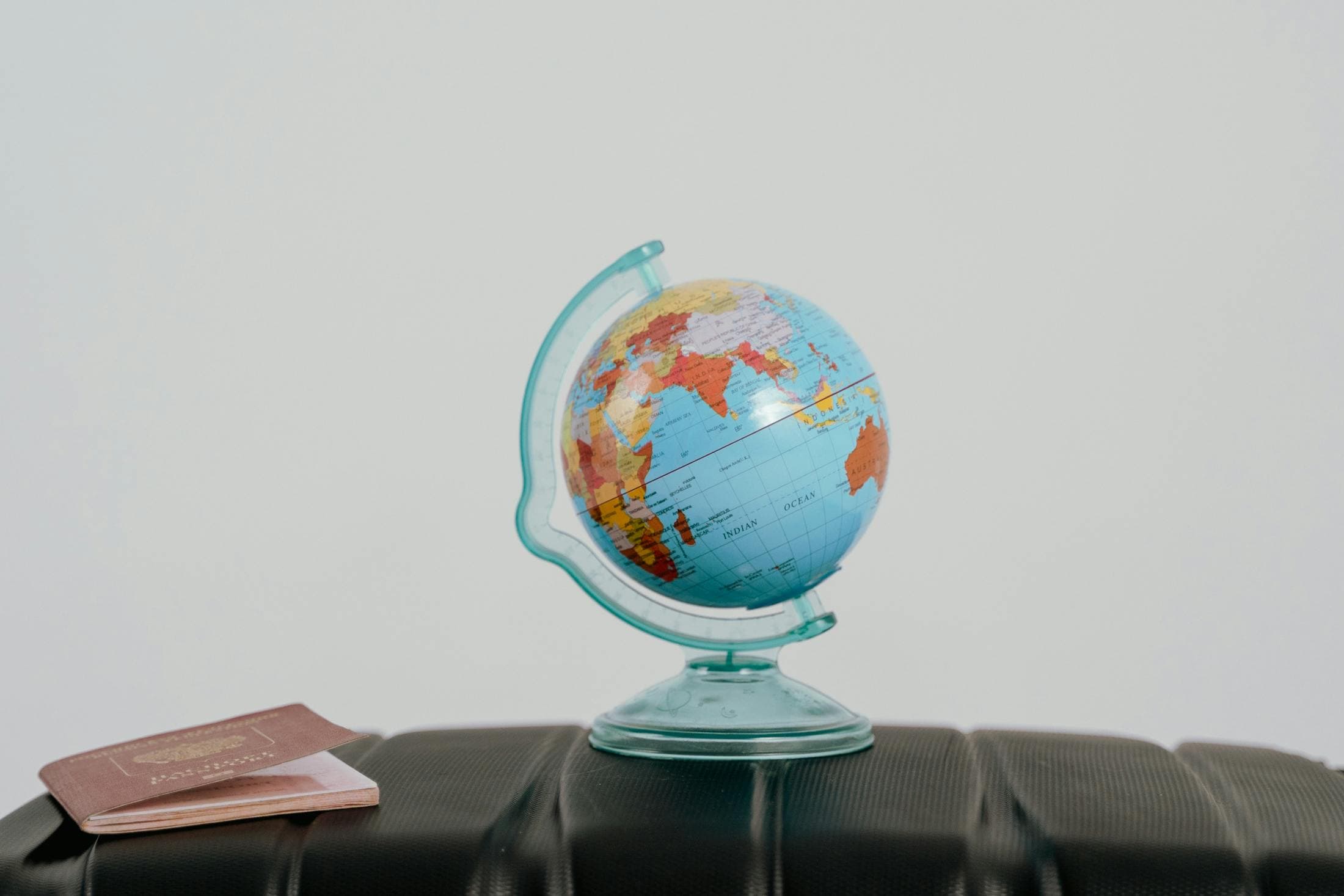Small globe resting on luggage beside a passport.