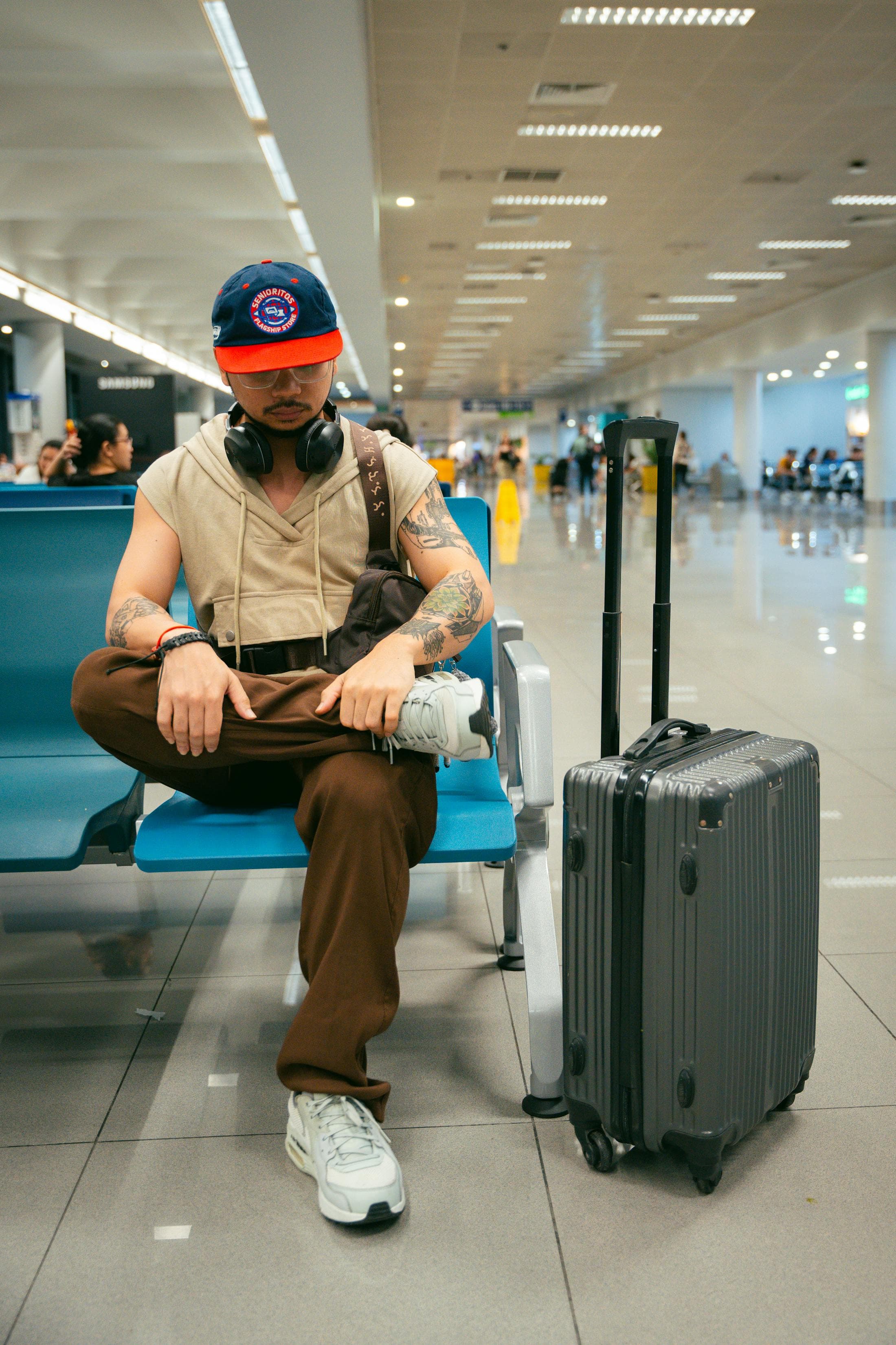 Traveler sitting in an airport terminal beside a suitcase.